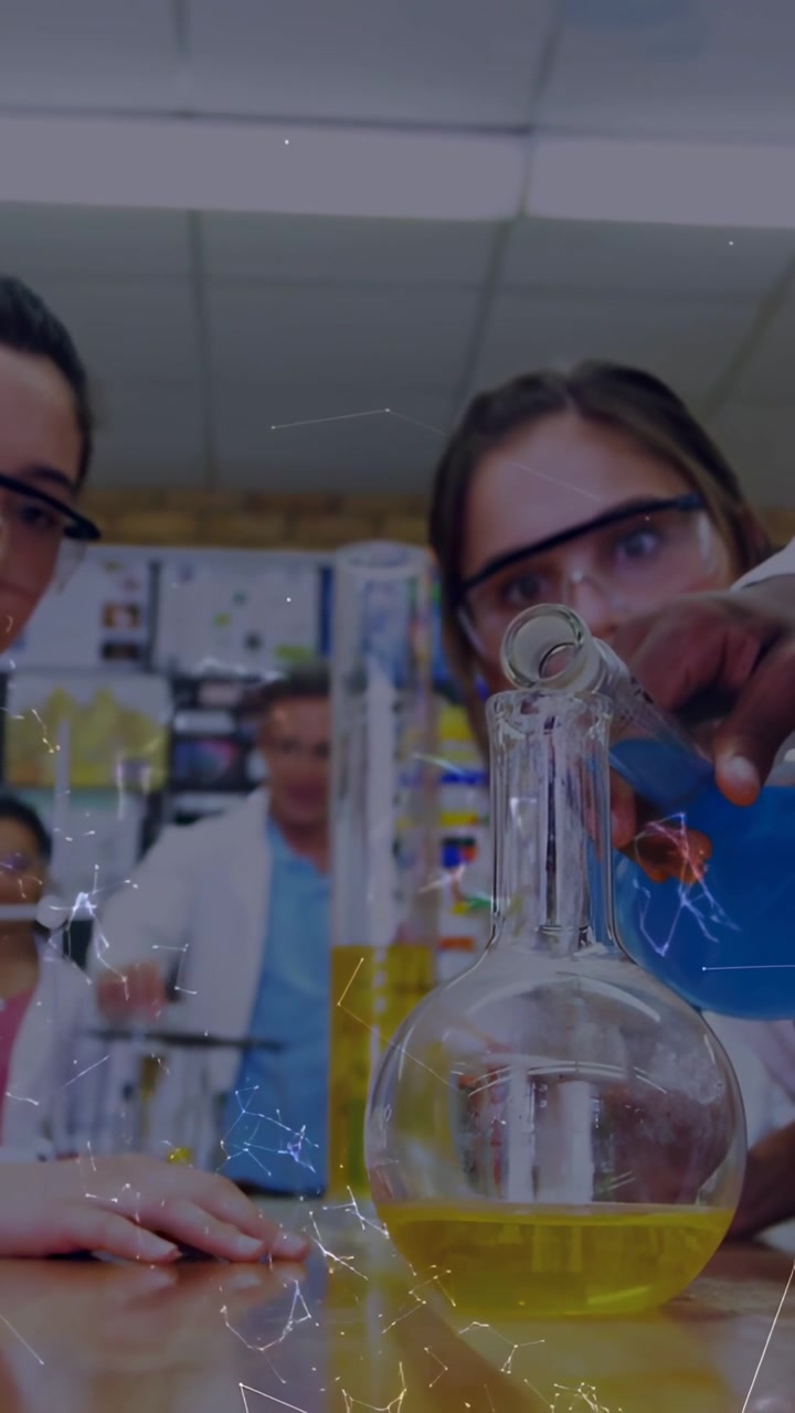 Vertical video: Students leaning as right student adding drops from pipette into flask during lab