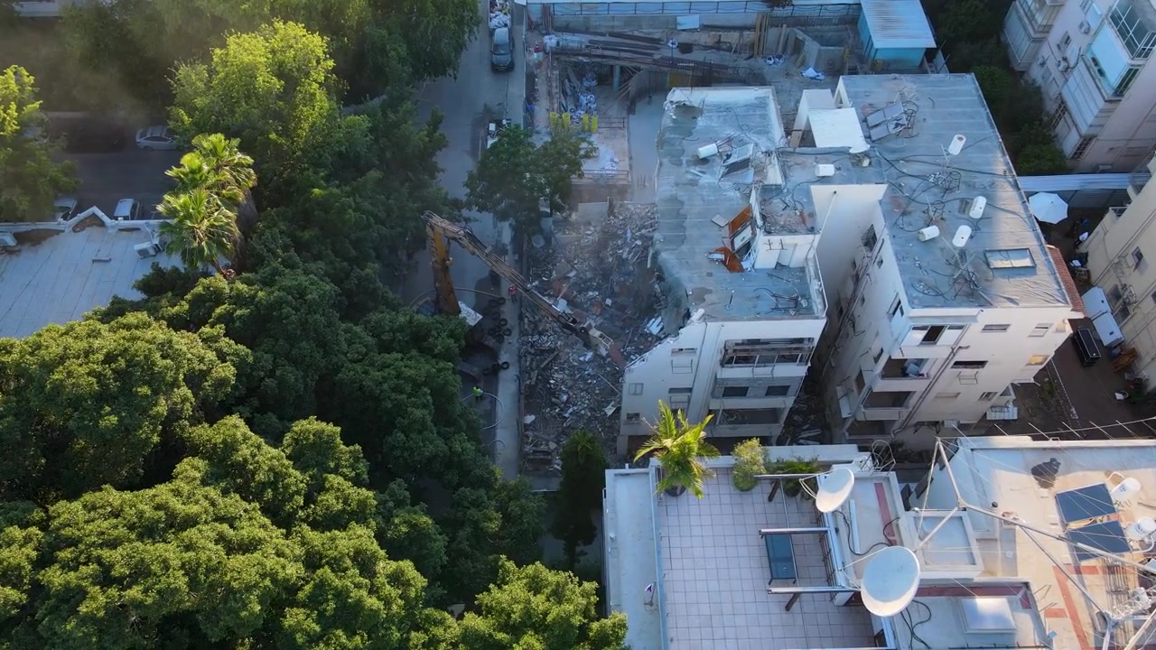 Perspectiva aérea de un bloque en reurbanización mostrando actividad de demolición y construcción, el dron desciende para establecer la toma.