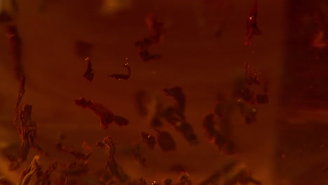 macro disparo de hojas de té de rooibos flotando en agua roja