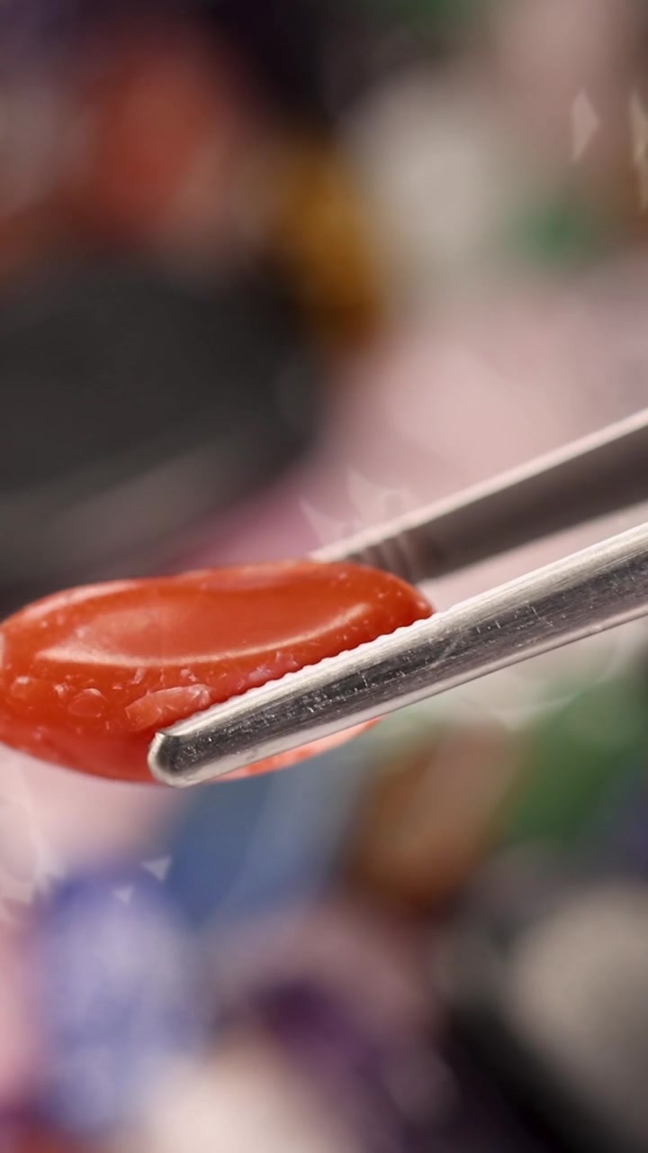 Macro view of tweezers picking up a red jasper stone from a colorful crystal collection.