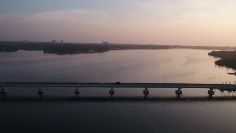 Aerial-of-indian-Kerala-bridge-over-wide-flowing-river-in-Kollam,-with-traffic,-cars-and-trucks,-crossing-at-sunset