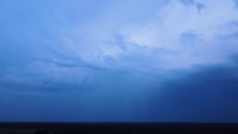 Beautiful-aerial-view-of-dramatic-dark-thunder-storm-clouds-in-summer-evening,-extreme-thunderstorm-with-spectacular-lightning-strike-flash-through-the-clouds,-distant-wide-angle-drone-tilt-up-shot