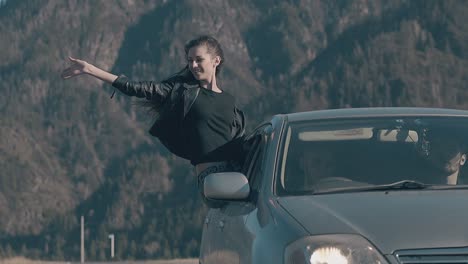 dark-haired-woman-leans-out-of-car-window-and-raises-hand