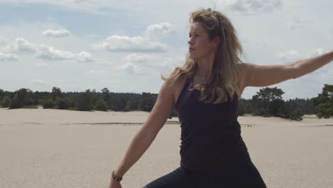 beautiful woman doing warrior pose in sand dunes