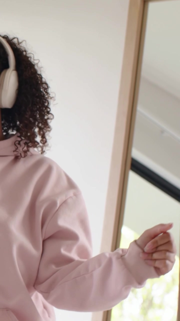 Video verticale: Ascoltando una canzone, una donna con felpa rosa apre una porta scorrevole a casa, con le cuffie.
