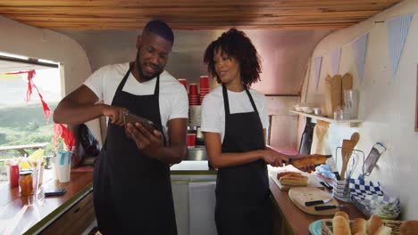 African-american-couple-wearing-aprons-using-digital-tablet-and-preparing-hot-dogs-in-the-food-truck