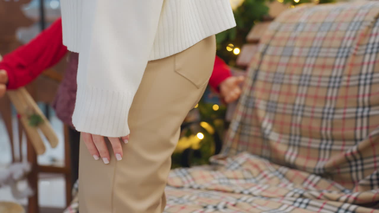 Close up of woman in brown trousers walking towards seat with christmas decoration, colorful lights and a festive atmosphere in shopping mall with trees and holiday ornaments