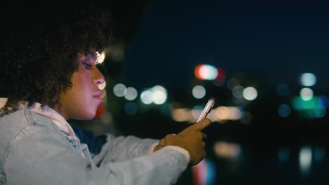 Mujer-Negra-Parada-En-El-Puente-Por-La-Noche-Y-Navegando-Por-Su-Teléfono-Móvil