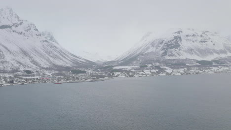 Ciudad-Costera-En-Kaafiord-Olddalen,-Noruega-Cubierta-De-Niebla-Durante-El-Invierno-Con-Montañas-Cubiertas-De-Nieve-En-El-Fondo---Toma-Aérea-En-Movimiento-Hacia-Adelante