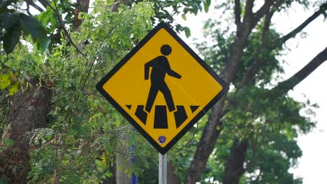 pedestrian crossing sign with lush green tree leaves on the background