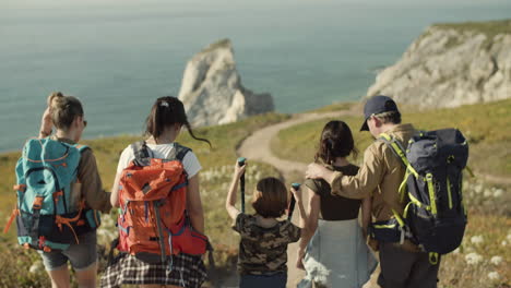 vista trasera de una familia caucásica con mochilas caminando por un camino de tierra hacia el mar