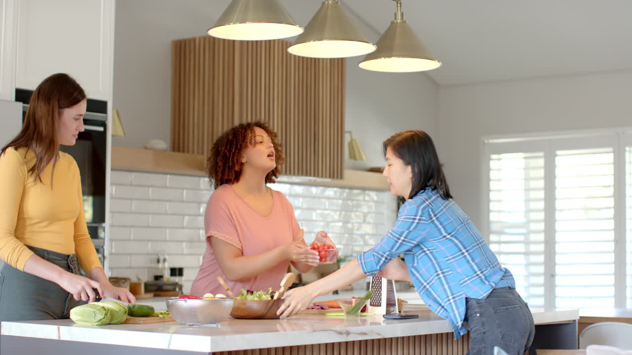 Preparing meal, three women friends chopping vegetables and grating cheese in kitchen