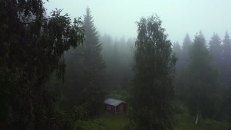 drone shot dolly out of a lonely log cabin in the middle of a cloud pine forest in unset norway