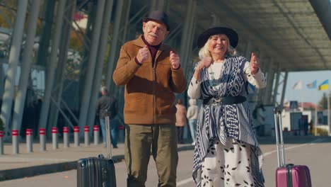 senior husband wife retirees tourists go to airport terminal for boarding with luggage on wheels