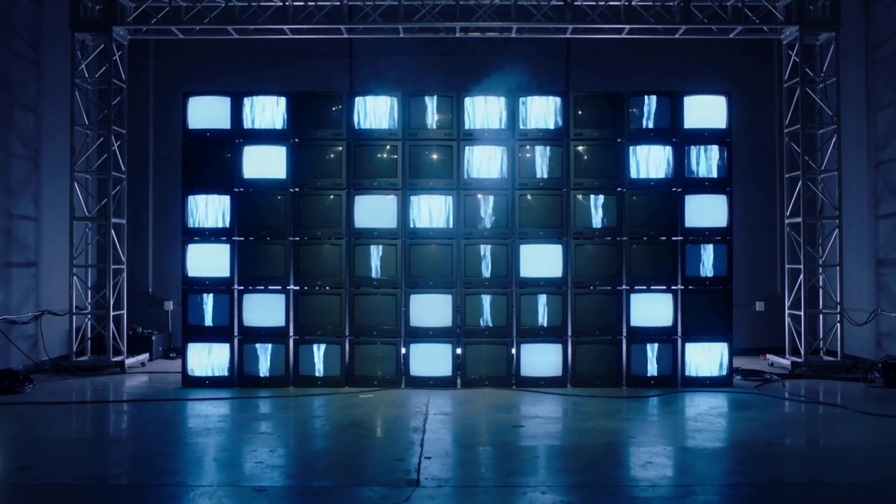 Lighting stacked CRT wall shifting into blue pattern in studio, truss, cables, floor reflecting