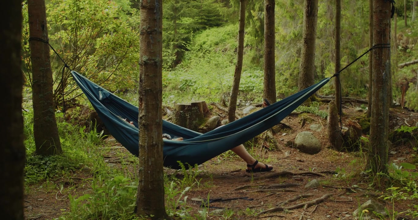Uma imagem serena de uma pessoa relaxando em uma rede azul, suspensa entre árvores em um cenário de floresta tranquila, perfeita para temas de relaxamento, natureza e bem-estar.