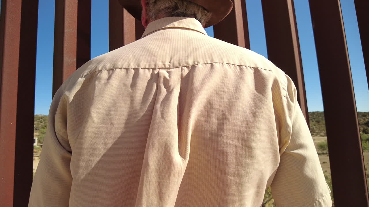 Man in hat peeks through US Mexico border fence