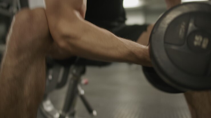 Muscular Man Performing Seated One-Arm Dumbbell Curls on Gym Bench
