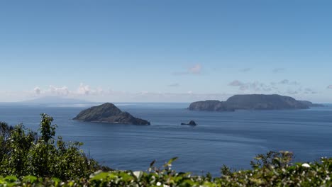 Timelapse-out-on-beautiful-blue-ocean-with-Tokyo-Islands,-vegetation-in-foreground-and-moving-clouds-on-sunny-day