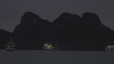 a tourist boat illuminated against the backdrop of a mountain in ha long bay, vietnam, at night