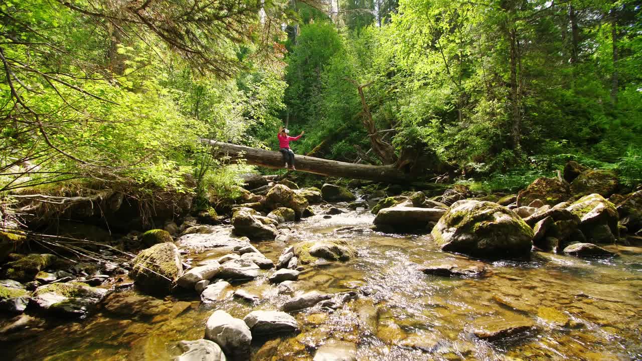 Person sitting on a fallen log in a mountain stream