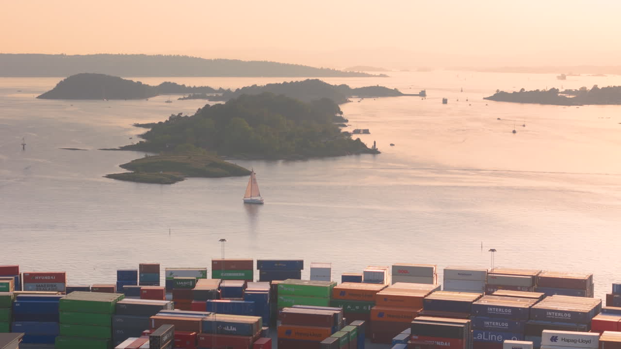 Sailboat at sunset cruise past container shipyard at Yilport Oslo, aerial view