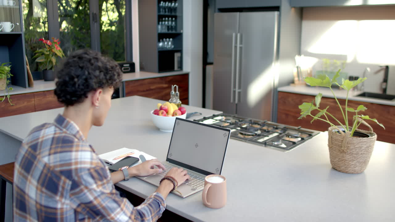 Working from home, teenage boy using laptop and smartphone in modern kitchen, copy space