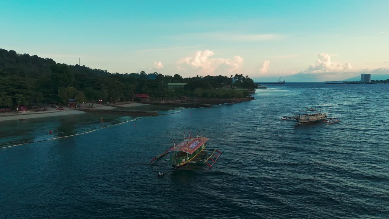 Aerial drone view of traditional fishing boats floating on the sea near a coastal shoreline with distant city skyline and colorful evening sky, perfect for travel, culture, lifestyle, and cinematic