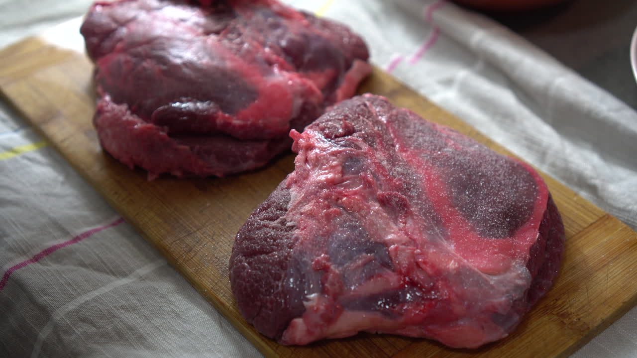 Pria Menaburkan Garam pada Sepotong Daging Lezat di Meja Dapur