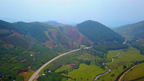 aerial drone shot of a winding highway and serpentine river passing through a fertile valley surrounded by green hills and scattered farms in southwestern uganda, near the kigezi highlands