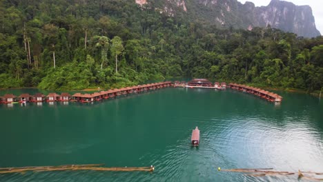 4k drone video of a boat sailing towards the floating bungalows in khao sok national park. these bungalows allow people top stay in the stunning nature of the national park.