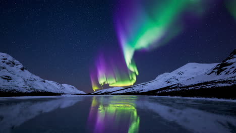 aurora borealis reflecting on a frozen lake with snow-capped mountains