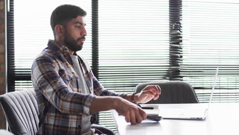 Young-Asian-businessman-in-a-plaid-shirt-uses-a-smartphone-in-an-office-setting-for-business-purpose