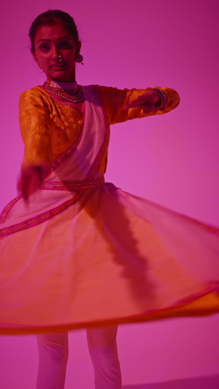 Vertical Video Of Spinning Female Kathak Dancer Performing Dance Wearing Traditional Indian Dress Against Purple Background 1