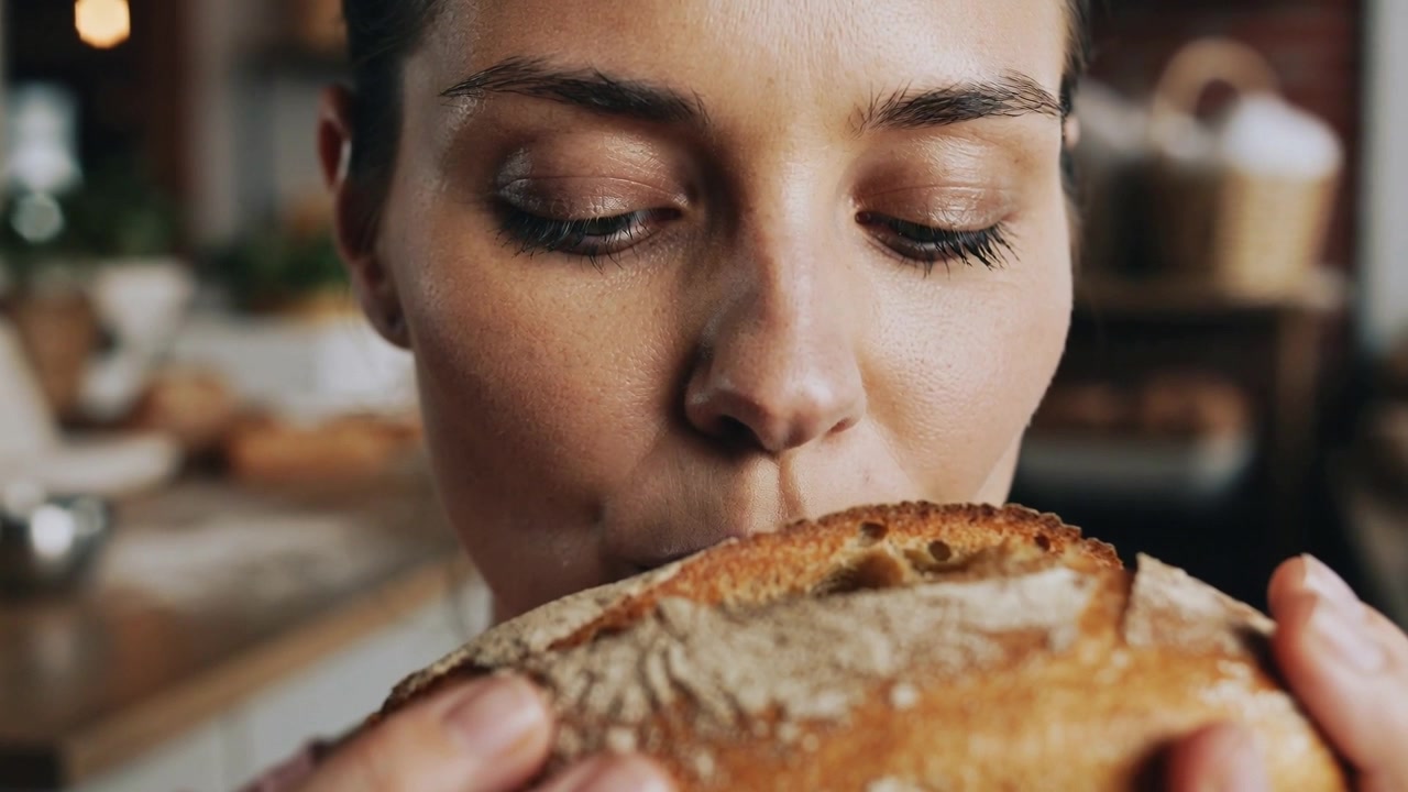 Smelling woman holding rustic loaf close at bakery counter, tasting crust and testing freshness