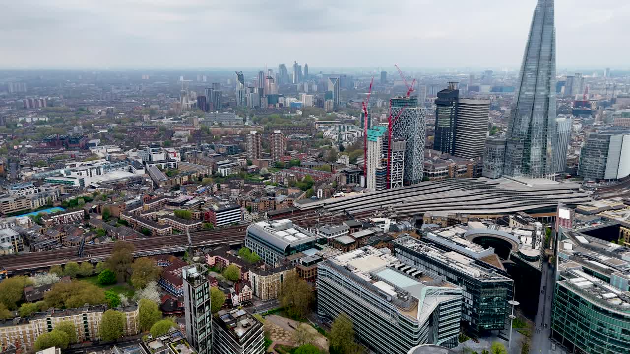 Incredible aerial drone footage captures a dramatic descent toward London Bridge station, with bustling trains below and the modern London skyline framed by soft clouds in the background.