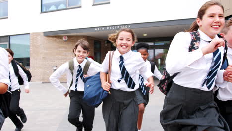 group of high school students wearing uniform running out of school buildings towards camera at the end of class