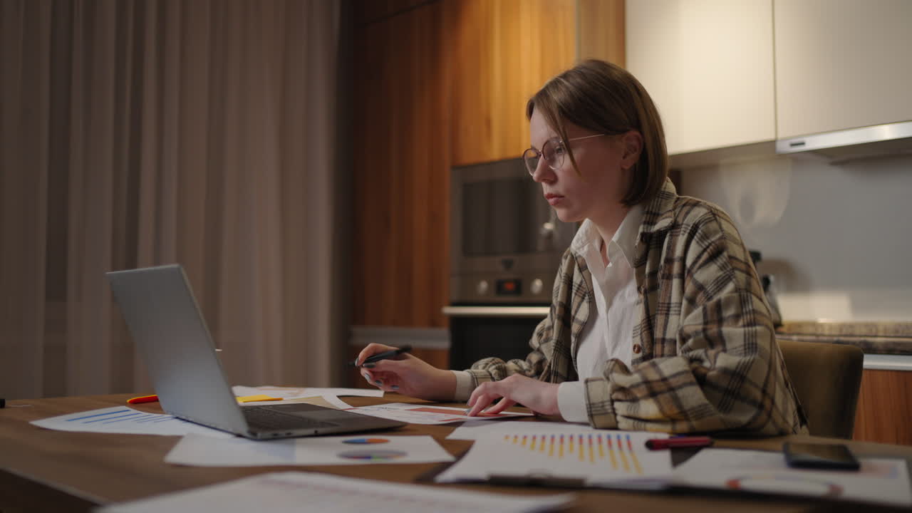 cámara de zoom una mujer con gafas trabaja remotamente desde casa sentada en una mesa con una computadora portátil y un bolígrafo marca los datos en el gráfico. el estudiante de aprendizaje a distancia en casa verá una conferencia