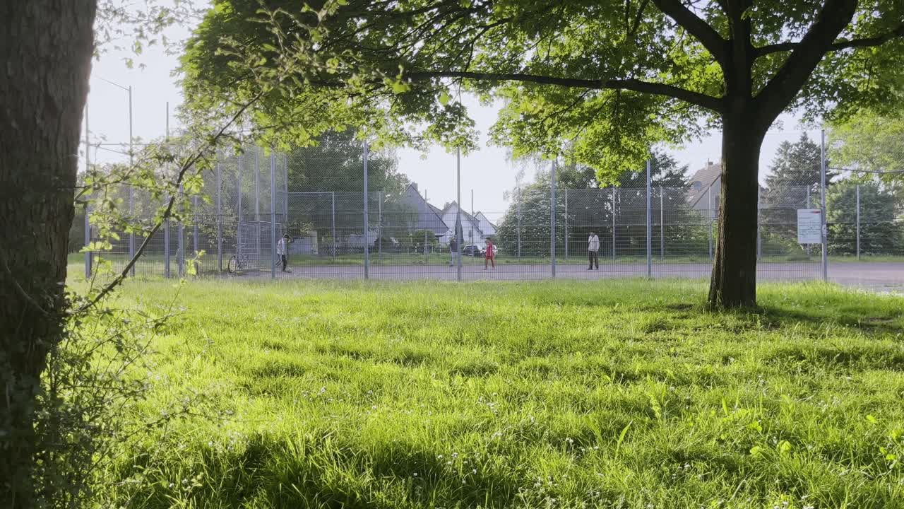 children play on a cinder football field in a residential area in cologne h&ouml;henhaus in the evening in the setting sun next to a meadow
