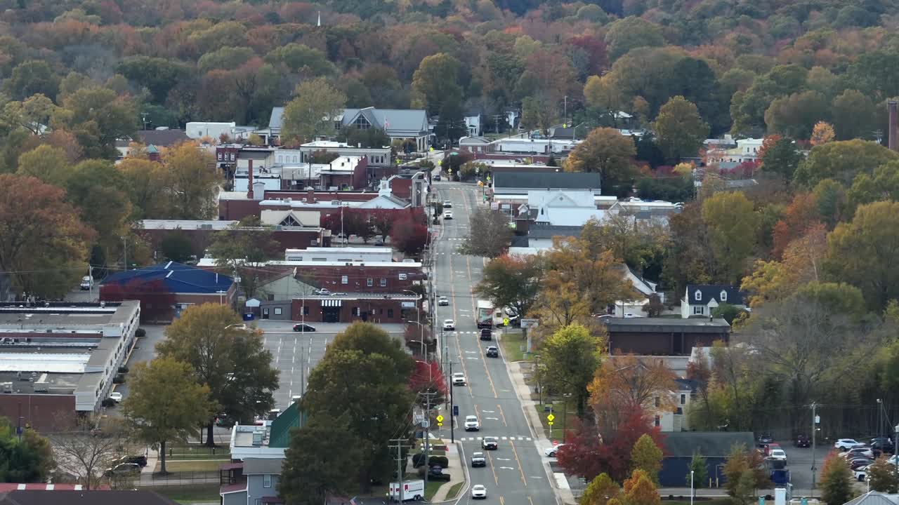 Traffic on Main Street of small American town on cloudy day in fall season. Red brick historic buildings and houses in city center. Virginia, USA. Aerial zoom wide shot