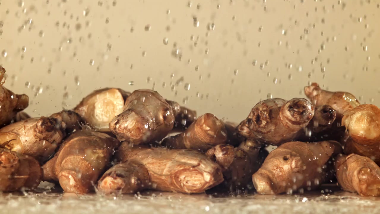 Gocce d'acqua che schizzano su radici di zenzero fresco al rallentatore