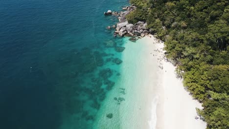 drone aerial over tropical blue clear water and white sandy beach with a foresty island