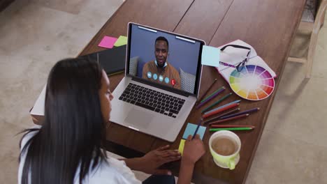 Caucasian-woman-using-laptop-on-video-call-with-male-colleague-and-making-notes