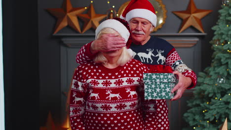 grandfather covering eyes of old grandmother with surprise christmas gift present box at home room