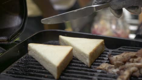 Buttering-white-toast-with-butter-knife-while-toasting-on-barbecue-grill,-filmed-as-close-up-shot-in-slow-motion