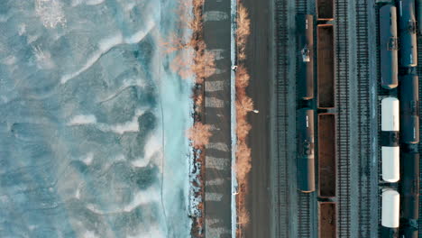 Aerial-shot-of-train-yard-by-walking-path-near-the-frozen-lake