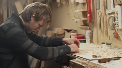 handheld shot young joiner working with piece of wood in workshop