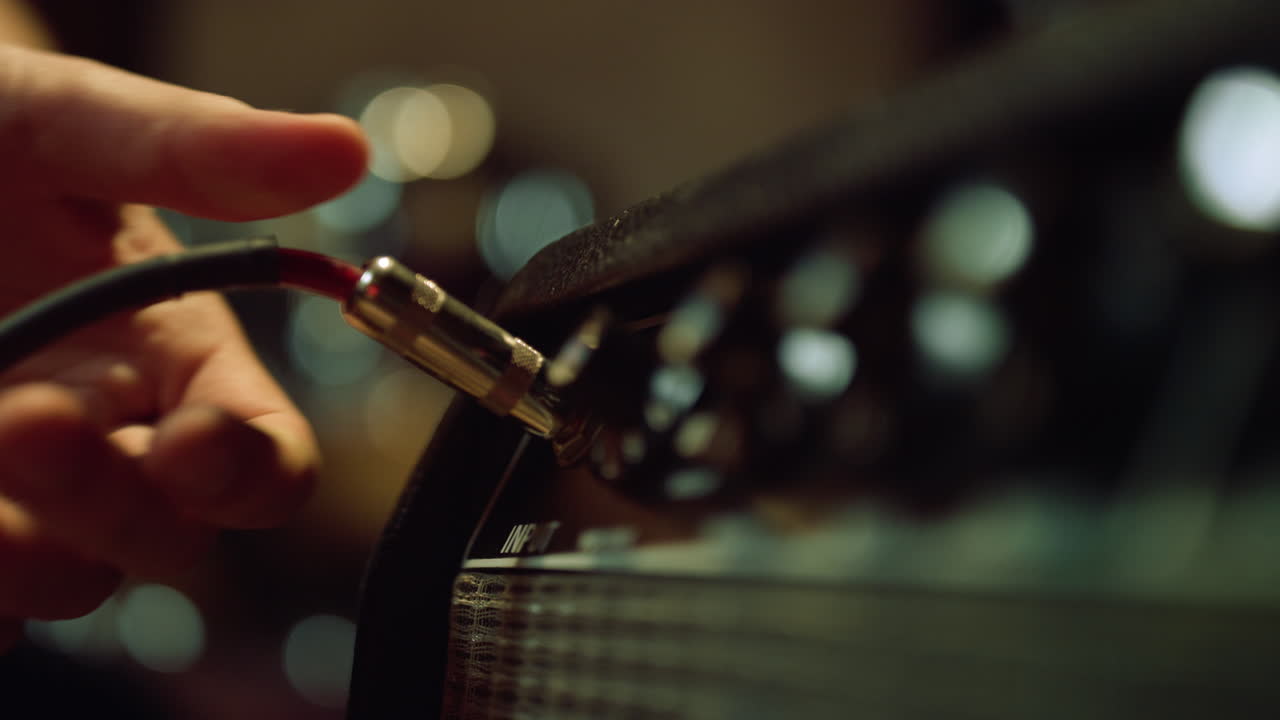 Sound engineer hand connecting plug to amplifier in late night recording studio.