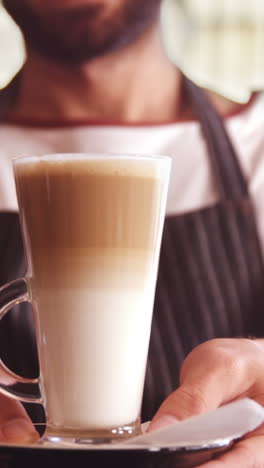 smiling waiter holding glass of cold coffee in cafe