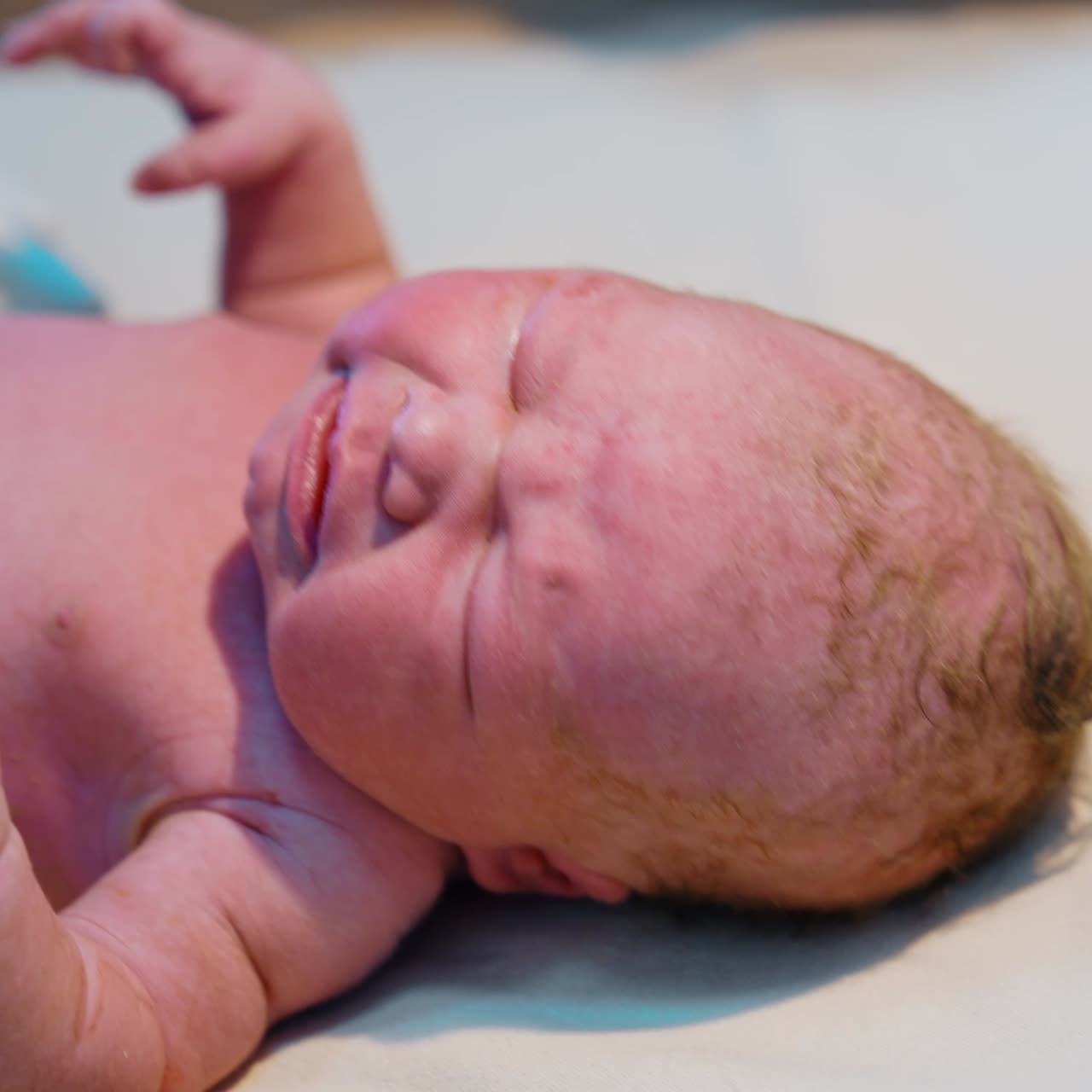 Few minutes old newborn with closed eyes doesn't like being examined by the doctor. Caucasian baby cries bitterly during check up. Close up